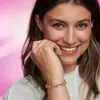 A woman smiling and touching her face, wearing a bracelet. Produktbild-Vorschau