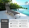 A grey sun lounger is placed on a patio next to a swimming pool with tropical plants in the background. Náhled obrázku produktu