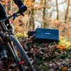 A person on a bicycle in a forest with a black case on the ground. Produktbild-Vorschau