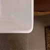 A close-up view of a white sink basin with a textured brown bath mat and a woven basket with a brown towel in the background. Produktbild-Vorschau