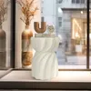 A white speckled side table with a U-shaped brown decorative object and a stack of books on top, placed near a window with a view of a city street. Anteprima dell’immagine prodotto