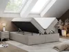 A bedroom with skylights, featuring a beige boxspring bed with its storage compartment open, revealing the mattress and internal storage space. A bedside table with a lamp is visible to the left, and decorative items are on the right. Produktbild-Vorschau