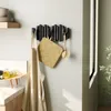 A kitchen wall with a black hook rack holding an apron, a pot holder, and a dish brush. A shelf with bowls is to the left, and a countertop with bottles is to the bottom left. Anteprima dell’immagine prodotto