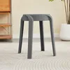 A gray stool sits on a textured rug in a room with a wooden shelf unit and a potted plant in the background. Anteprima dell’immagine prodotto