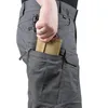 A close-up of a person's hand reaching into the cargo pocket of gray tactical pants, holding a flashlight and a tan wallet. Náhled obrázku produktu