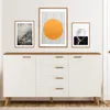 A white sideboard with wooden accents and three framed pictures on the wall above it. Náhled obrázku produktu