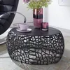 A round coffee table with a decorative base, set in a living room with a chair and decorative items on top. Anteprima dell’immagine prodotto
