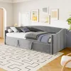 A gray upholstered daybed with a pull-out trundle is set up in a bedroom with artwork on the wall. Produktbild-Vorschau