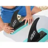 A person is attaching fins to a stand-up paddleboard on a beach. Produktbild-Vorschau