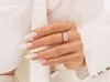 A close-up shot of a woman's hand wearing a ring and showing off her nails, which are painted in a soft pink color. She is wearing a white blazer. Anteprima dell’immagine prodotto