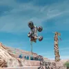 An RC car is captured mid-air, upside down, performing a stunt over a graffiti-covered set of stairs in a desert-like environment with a palm tree in the background. Náhľad obrázku produktu