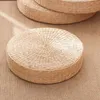 A round, woven straw cushion is placed on a textured brown mat. Another similar cushion is visible in the background. Produktbild-Vorschau