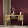 A wooden desk with rattan details is shown against a burgundy wall and a slatted wooden panel. Produktbild-Vorschau