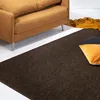 A close-up view of a dark brown rug in a living room setting, with a corner of a brown sofa and two pillows visible. Náhled obrázku produktu