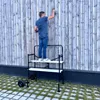 A man is standing on a mobile scaffolding unit and painting a wooden fence. Anteprima dell’immagine prodotto