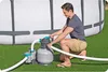 A man is kneeling next to a pool pump and filter system, adjusting a valve. The pool is in the background. Produktbild-Vorschau