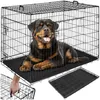 A Rottweiler dog is lying inside a black wire dog crate. The crate is shown from the front and slightly to the side. A second, disassembled crate and a tray are shown in the foreground. Produktbild-Vorschau