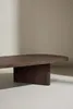 A close-up shot of a modern, dark wood coffee table with an oval top and a single, thick pedestal base, set against a neutral, softly lit background. Produktbild-Vorschau