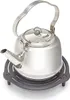 A stainless steel kettle sits on a black trivet. Produktbild-Vorschau
