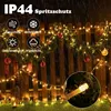 A string of warm white fairy lights is draped over a wooden fence, decorated with pine garland and Christmas ornaments. The image is set outdoors, possibly during rain, as indicated by the text and visual cues. Náhled obrázku produktu