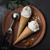 Two ice cream cones and an ice cream scoop on a wooden board with scattered nuts and leaves. Náhľad obrázku produktu