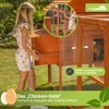 A young girl is interacting with a wooden chicken coop in a grassy outdoor setting. Produktbild-Vorschau