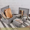 Two grey storage boxes filled with kitchen items like cutting boards, rolling pins, jars, and spice grinders, placed on a patterned rug. Produktbild-Vorschau