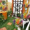 A vibrant garden scene with numerous artificial flower arrangements in pots and baskets, placed on a grassy area with decorative stepping stones and a wooden cabinet. Produktbild-Vorschau
