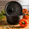 A black cast iron pot with its lid slightly ajar, placed on a wooden surface with red bell peppers and bay leaves. Náhled obrázku produktu