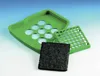 A green plastic tray with circular cutouts, a smaller green plastic grid, and a black square filter are arranged on a light blue and white background. Anteprima dell’immagine prodotto