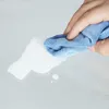 A hand is wiping a white liquid spill on a light gray surface with a blue microfiber cloth. Náhľad obrázku produktu