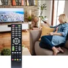 A woman is sitting on a couch in a living room, holding a remote control and pointing it towards a TV. Podgląd zdjęcia produktu