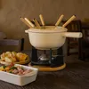 A fondue set with accompanying food items is arranged on a wooden table. Voir les images du produit