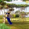 A wooden playground set with a slide, swings, and climbing wall is set up on a grassy lawn surrounded by trees. Podgląd zdjęcia produktu