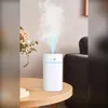 A white aroma diffuser humidifier is placed on a wooden table, emitting a mist. A bouquet of dried flowers is to the left, and a dark gray sofa is in the background. Produktbild-Vorschau