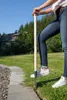 A person is using a garden tool to edge a lawn next to a stone path. A house and trees are in the background. Produktbild-Vorschau