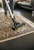 A person is vacuuming a rug with a cordless vacuum cleaner. Produktbild-Vorschau