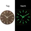 A split image showing a wooden wall clock in daylight on the left and the same clock at night with its luminous features glowing on the right. Produktbild-Vorschau