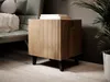 A wooden nightstand with a fluted front is placed next to a chair and a plant. Náhled obrázku produktu
