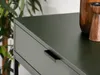 A close-up shot of a dark green console table with a black drawer pull, with a plant in the background and wooden decorative items on the table. Produktbild-Vorschau