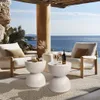 A stylish outdoor patio with two white textured chairs, two white speckled side tables, and a bottle of wine with glasses, overlooking a calm blue ocean. Podgląd zdjęcia produktu