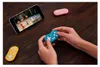 A person is playing a game on a smartphone using a small turquoise gamepad. Other gamepads are visible on a wooden table. Náhľad obrázku produktu