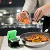 A person is adding chopped ingredients to a pan of shrimp and lemon slices cooking in a kitchen. Produktbild-Vorschau