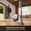 A person walks through a doorway while a vacuum cleaner stands upright in the foreground, with a close-up inset showing a feature. Produktbild-Vorschau
