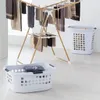 A wooden drying rack with clothes hanging on it, and two laundry baskets, one empty and one with a folded towel, are shown on a light-colored floor. Produktbild-Vorschau