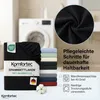A folded black fitted sheet is shown in the foreground, with a stack of fitted sheets in various colors behind it. A washing machine is visible in the background. Close-up of the fabric texture is shown in a circle. Produktbild-Vorschau