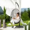 A woman sits in a hanging chair outdoors, holding a drink. The background shows a lush green landscape with mountains. Náhled obrázku produktu
