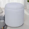 A white, textured, cylindrical ottoman sits on a light-colored floor. To the left are two grey toy-like objects with wheels. In the background, a white curtain and a white vase with a smiley face are visible. Náhled obrázku produktu