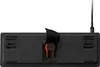 The underside of a black gaming keyboard with a cable attached and an orange accent piece visible. Produktbild-Vorschau