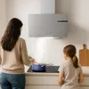 A woman and a child are in a modern kitchen, with the woman cooking on a stovetop under a sleek range hood. Náhled obrázku produktu
